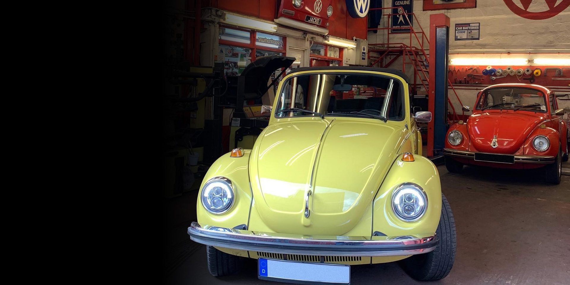 A classic yellow VW Beetle convertible in the Jack's Garage workshop, with a red Beetle alongside